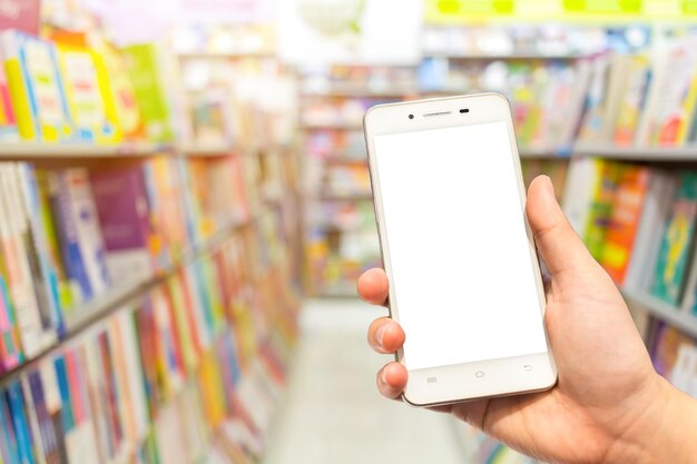 Mano cortada de una persona que usa un teléfono móvil contra una estantería en una tienda