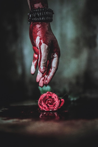 Mano cortada de una persona con sangre llegando a la rosa en el suelo