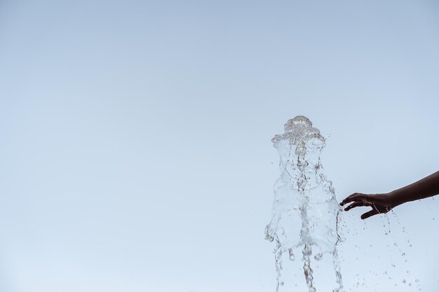 La mano cortada de una persona tocando el salpicamiento de agua contra un cielo despejado