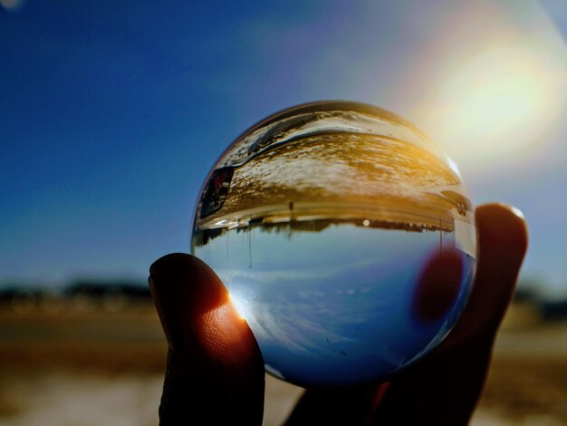 Foto mano cortada sosteniendo una bola de cristal contra el cielo