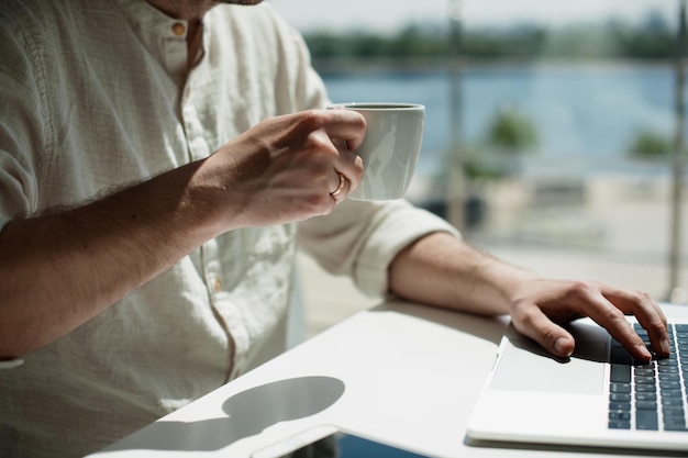 Mano cortada sosteniendo café mientras usa una computadora portátil en la mesa en un restaurante