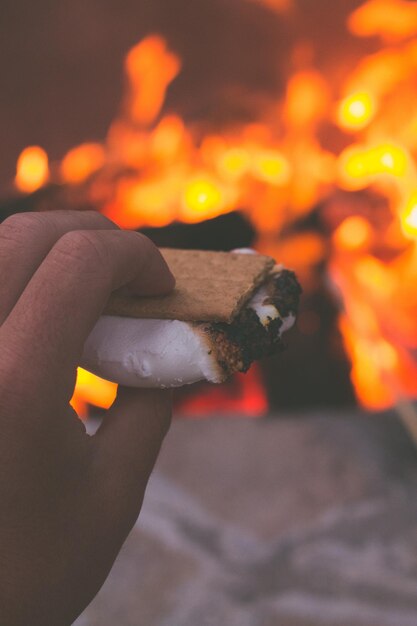 Foto mano cortada sosteniendo comida junto a la hoguera por la noche