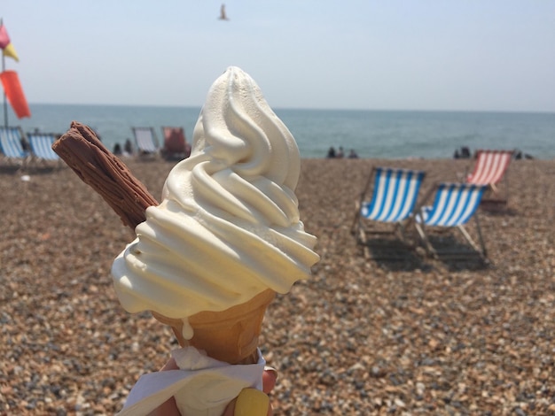 Foto mano cortada sosteniendo un cono de helado en la playa en un día soleado