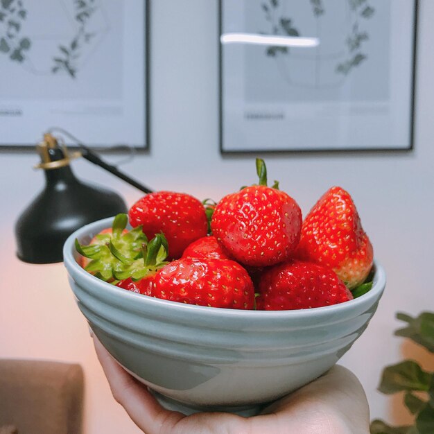 Foto mano cortada sosteniendo fresas en un cuenco en casa