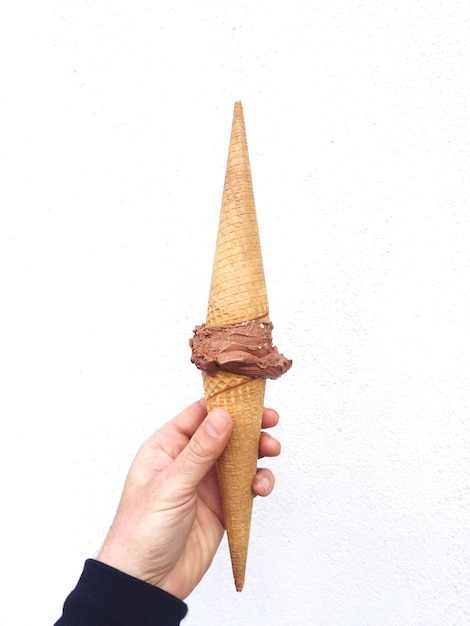 La mano cortada sosteniendo el helado contra la pared
