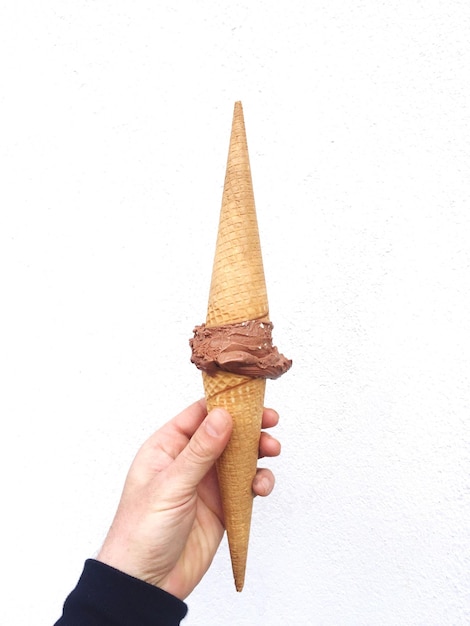 Foto la mano cortada sosteniendo el helado contra la pared