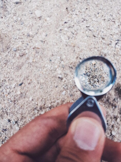 Foto mano cortada sosteniendo una lupa en la arena de la playa