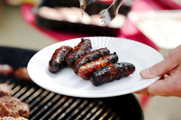 Mano cortada sosteniendo salchichas de barbacoa en un plato