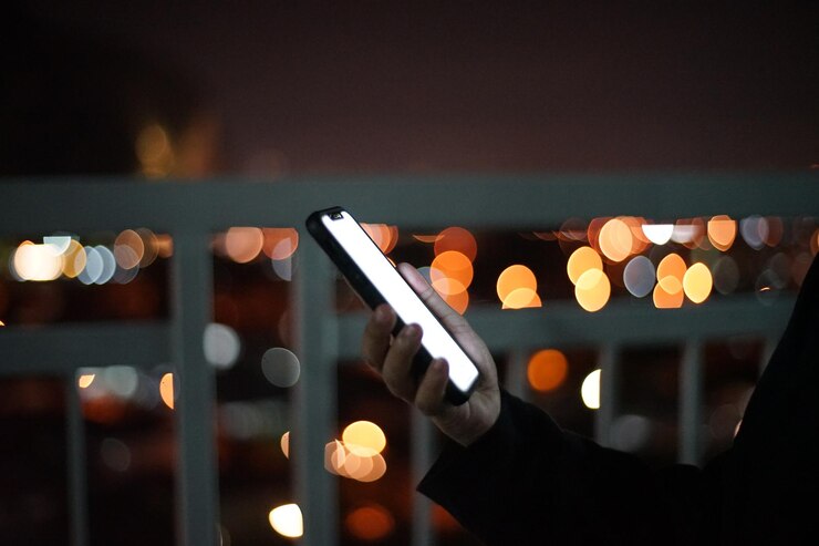 Foto mano cortada sosteniendo un teléfono móvil contra luces desenfocadas por la noche