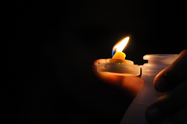 Mano cortada sosteniendo una vela encendida en el cuarto oscuro