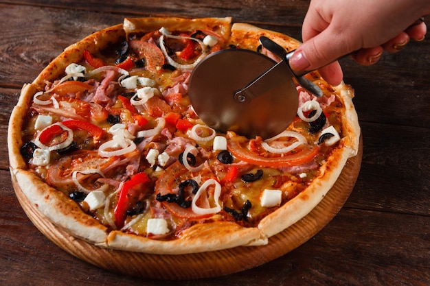 Foto mano cortando deliciosa pizza servida en mesa rústica de madera, de cerca. cocina tradicional italiana, comida rápida.