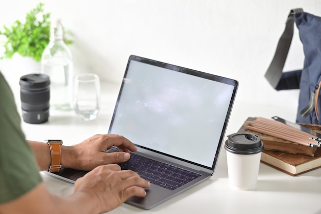 Mano cosechada del hombre de negocios del tiro que trabaja con su computadora portátil en espacio de trabajo del escritorio