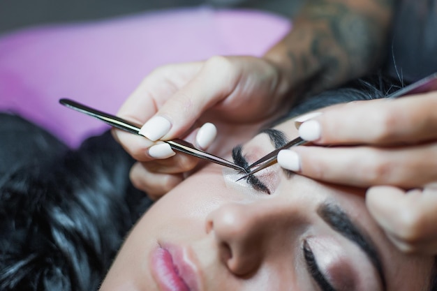 La mano de la cosmetóloga hace la extensión de pestañas con un cepillo de pestañas de cerca