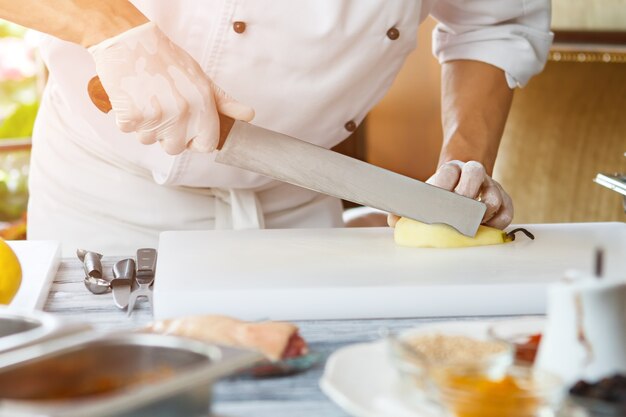 Mano con cuchillo corta pera pera en blanco tablero de cocina cafe chef prepara fruta fresca sólo ingredientes