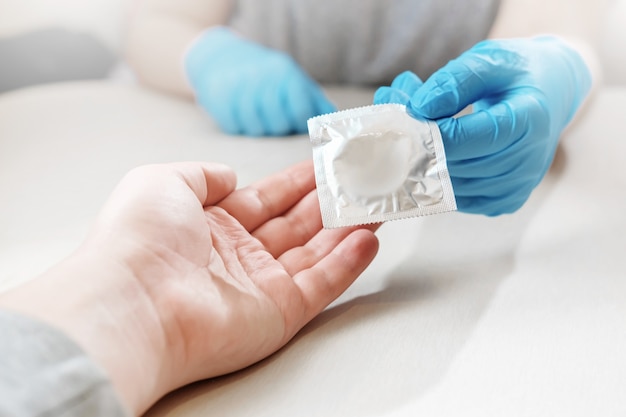 Foto la mano le da al brazo un condón, el médico le da un condón, las manos en guantes, protección contra el embarazo, anticonceptivo, manos y condón, desde la primera persona