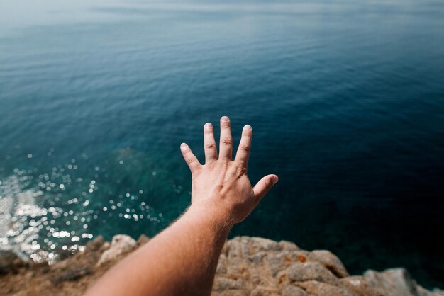 Mano de homem de perto contra a água azul clara do mar Mediterrâneo Vista do penhasco Grécia