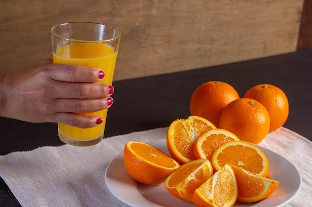 Mano de mujer sostiene un vaso de jugo em uma mesa, fondo de fruta de naranja saludable muchas frutas frescas de naranja, vida sana.