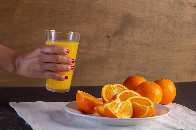 Mano de mujer sostiene un vaso de jugo en una mesa, Fondo de fruta de naranja saludable muchas frutas frutas frescas de naranja, vida sana.