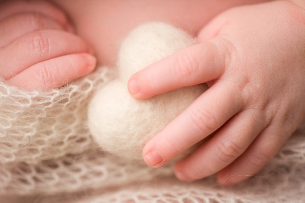 La mano y los dedos de un bebé recién nacido. La mano y los dedos de un bebé recién nacido. Un bebé sostiene un corazón blanco tejido con sus dedos.