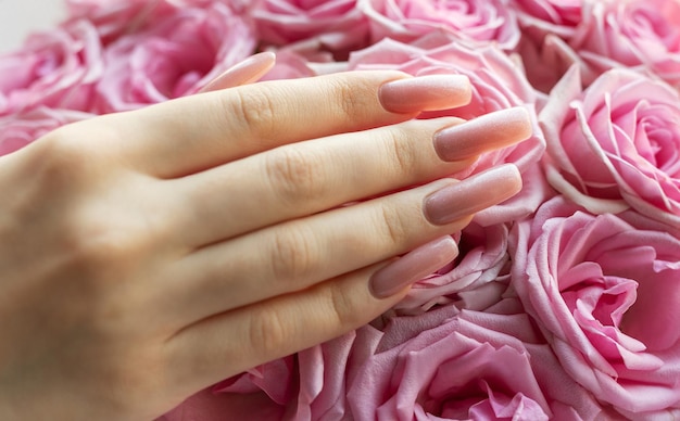 Una mano delicada con uñas pulidas descansando suavemente sobre rosas rosadas vibrantes