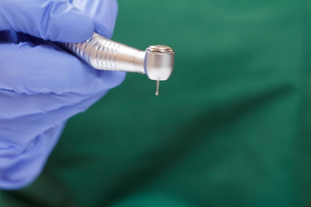 La mano del dentista en un guante de látex azul con una nueva pieza de mano dental de alta velocidad en un fondo borroso