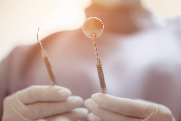 La mano del dentista sostiene el comprobador de dientes y un espejo para revisar y cuidar las herramientas y el equipo del dentista.