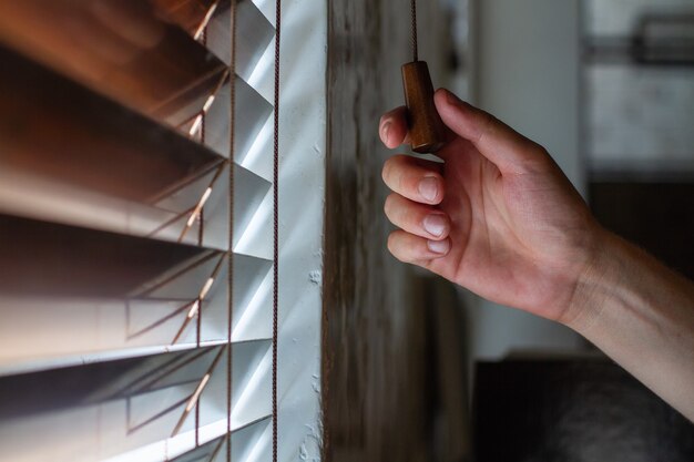 Foto la mano derecha del hombre sostiene una de las cuerdas de control de las contraventanas de madera de la ventana.