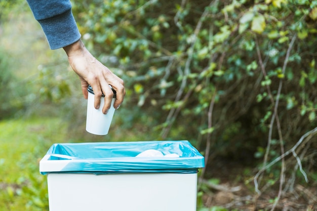 Mano deshacerse de una taza de papel en la basura