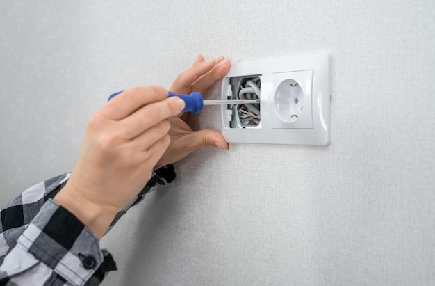 Foto mano con destornillador para reparar tomas eléctricas en casa el electricista está usando un destornillador para instalar una toma de corriente en una caja de plástico en una pared blanca