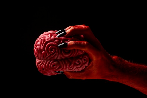 Mano del diablo rojo sosteniendo un concepto de Halloween del cerebro humano