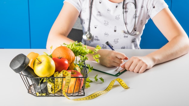Foto mano de dietista femenina cerca de frutas sanas y pesas en bandeja
