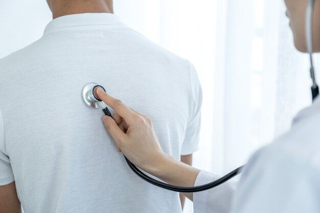 Foto mano doctora examinando la salud de los pacientes masculinos con un estetoscopio.