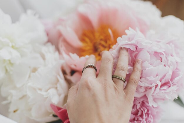 Mano con elegantes anillos en un hermoso ramo de peonías Imagen tierna Elementos esenciales femeninos