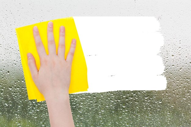 Foto la mano elimina las gotas de lluvia sobre el vidrio con un trapo amarillo