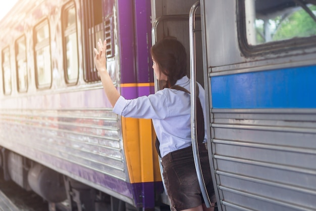 La mano embarazada de la mujer asiática dice hola y el bolso rojo en el tren de la estación de tren del viaje tra