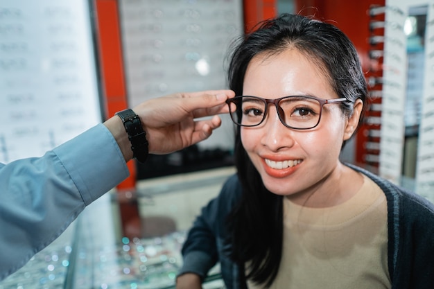 La mano de un empleado está ayudando a ponerse un par de anteojos que una mujer que se ha realizado un examen de la vista ha elegido en una clínica oftalmológica