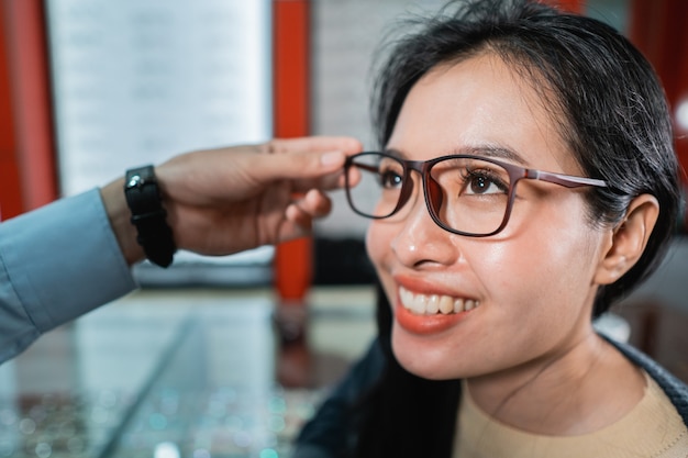 La mano de un empleado está ayudando a ponerse un par de anteojos que una mujer que se ha realizado un examen de la vista ha elegido en una clínica oftalmológica