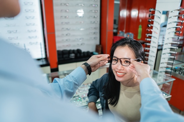 La mano de un empleado está ayudando a ponerse un par de anteojos que una mujer que se ha realizado un examen de la vista ha elegido en una clínica oftalmológica