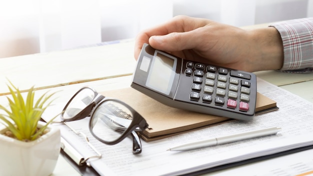 La mano del empleado masculino sostenga la pluma de plata usando la calculadora para evaluar los gastos