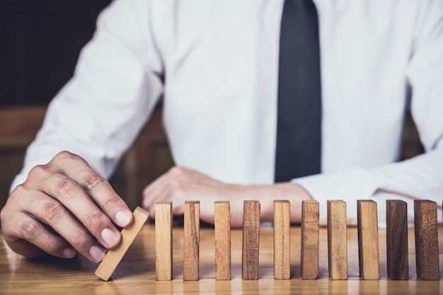 Mano de empresario detener el efecto de dominó de madera cayendo desde continuo derrocado o riesgo