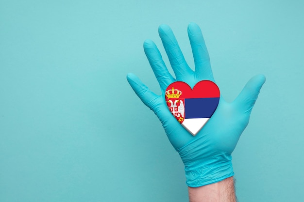 Mano de enfermera de corazón de salud médica de serbia sosteniendo la bandera del corazón del país