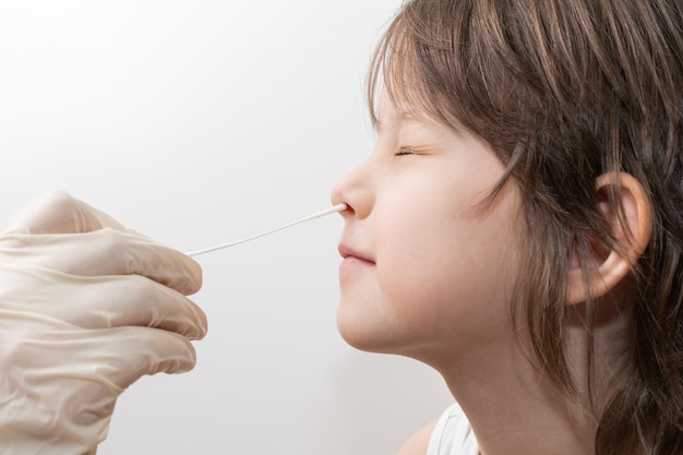 la mano de una enfermera con guantes de látex inserta un hisopo en la nariz de un niño para recolectar una muestra de COVID19