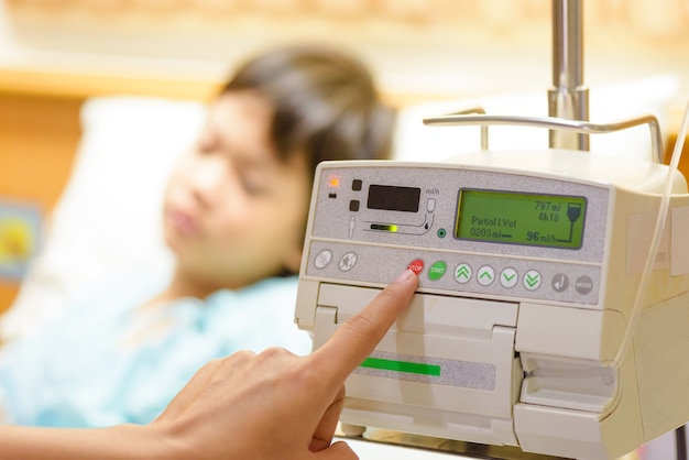 La mano de la enfermera que presiona en la bomba de la infusión intravenosa IV gotea con el fondo admitido cabrito.