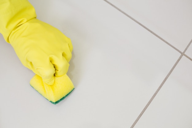 Mano enguantada amarilla con esponja limpiando el piso