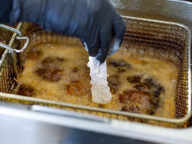 La mano enguantada del chef sumerge un trozo de pollo en el aceite burbujeante.