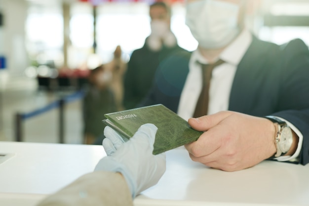 Mano enguantada de la recepcionista que devuelve el pasaporte del elegante empresario sobre el mostrador de recepción después del registro antes del vuelo