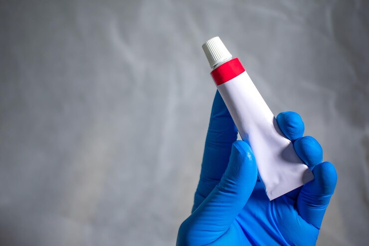 Foto la mano enguantada sostiene y presenta un tubo cerrado de ungüento médico. concepto de publicidad médica