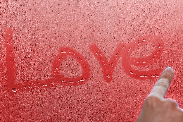 Mano escribe amor en el cristal de la ventana con fondo de gotas