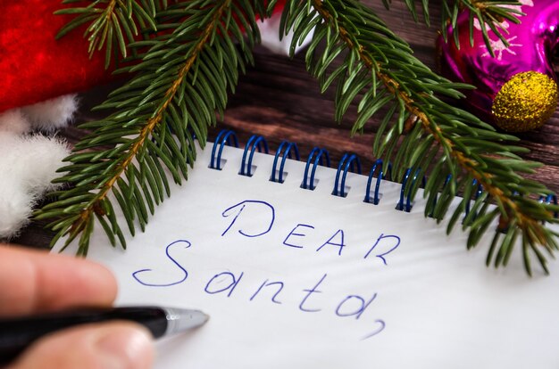 Foto mano escribe una carta a santa estimado santa escrito en un bloc de notas y adornos navideños closeup