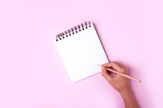 Mano escribe con un lápiz en un cuaderno sobre un fondo rosa. Concepto también lista de cosas